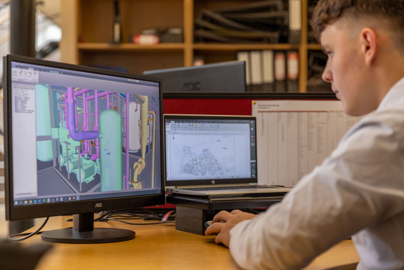 Engineer reviewing a 3D CAD model and site plan on dual screens